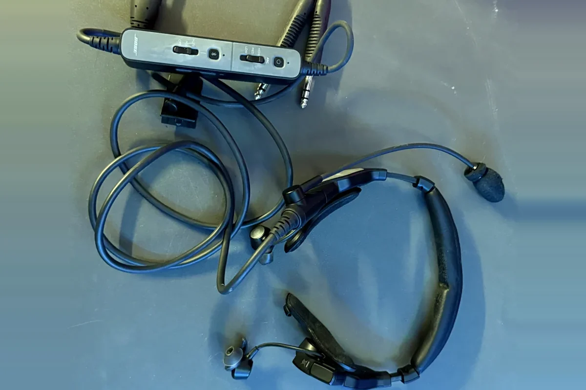 Bose ProFlight Series 2 posé à plat : boîtier de commande avec les trois niveaux de réduction de bruit, prises, micro à perche, embouts intra-auriculaires et arceau de nuque fin et peu garni (photo personnelle)